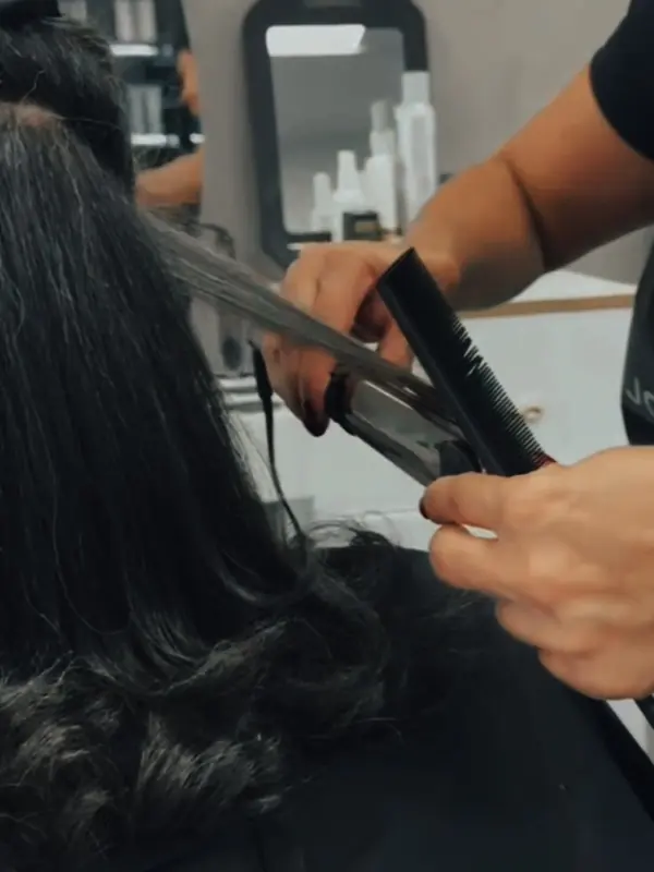 A stylist using a flat iron on a client’s long hair